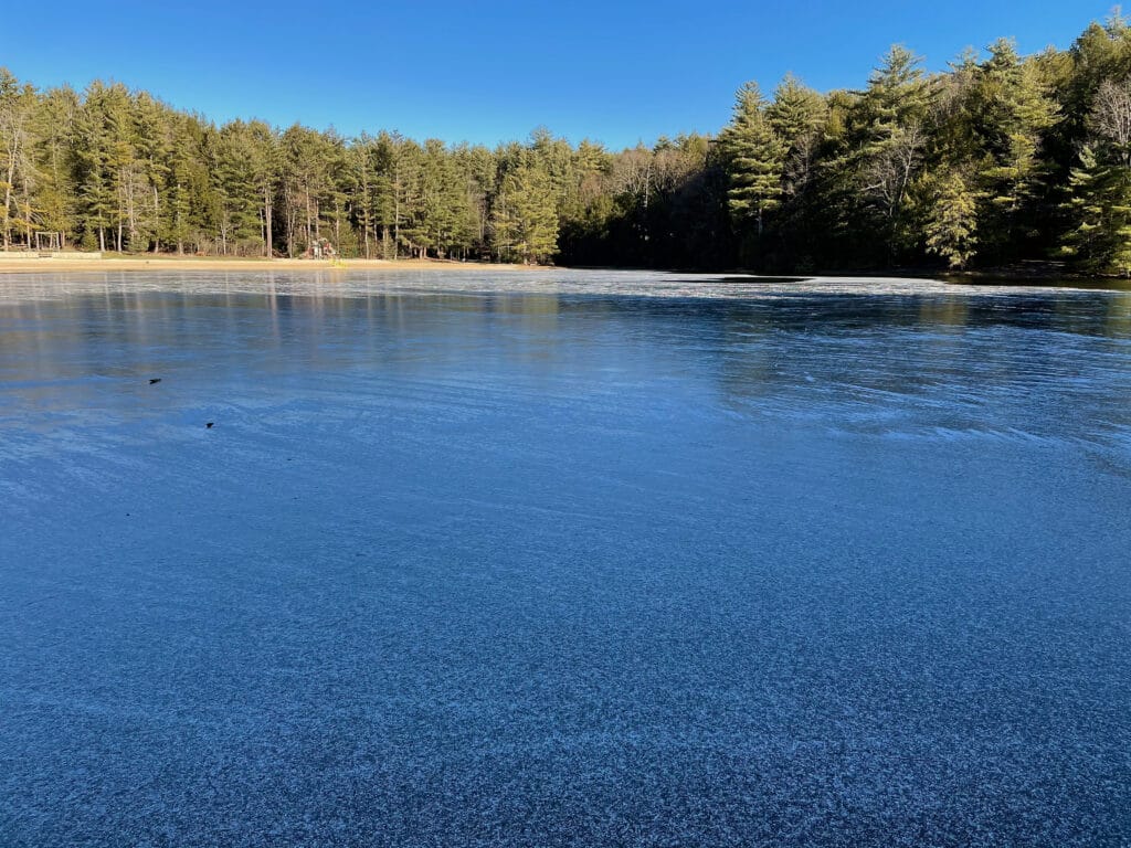The lake is frozen over, with a light dusting of snow on top of the ice.
